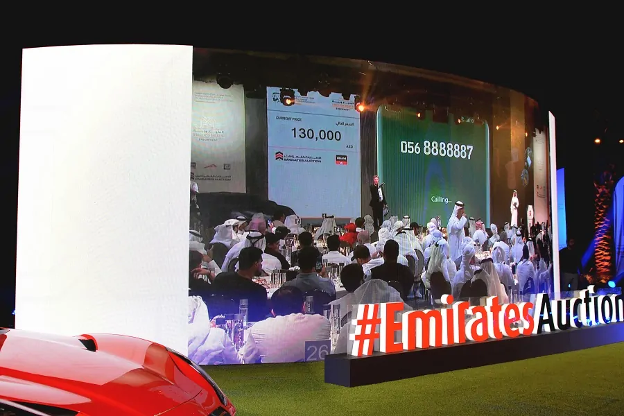 Bidders before a curved LED wall showing live bids at the Emirates Auction charity number-plate auction in Dubai 2023, by Topaz Events