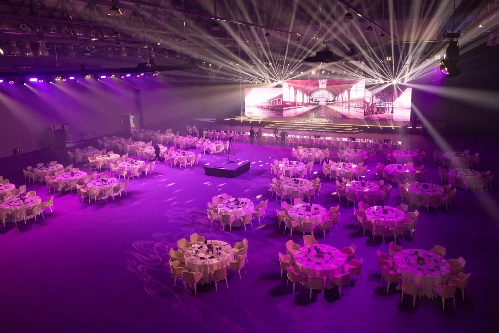 Wide view of the Expo Centre Sharjah hall set with round tables in pink and purple lighting for Shjseen 2026