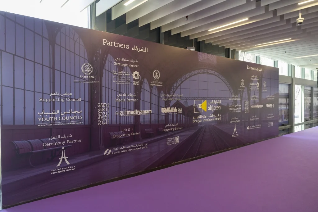 Partners wall with sponsor logos and Sharjah Excellence Award artwork at the event entrance