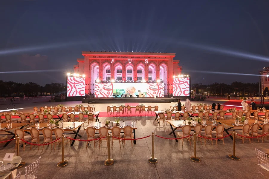 AUS main building lit red with LED stage and gala dinner seating at the American University of Sharjah Alumni Gala 2025