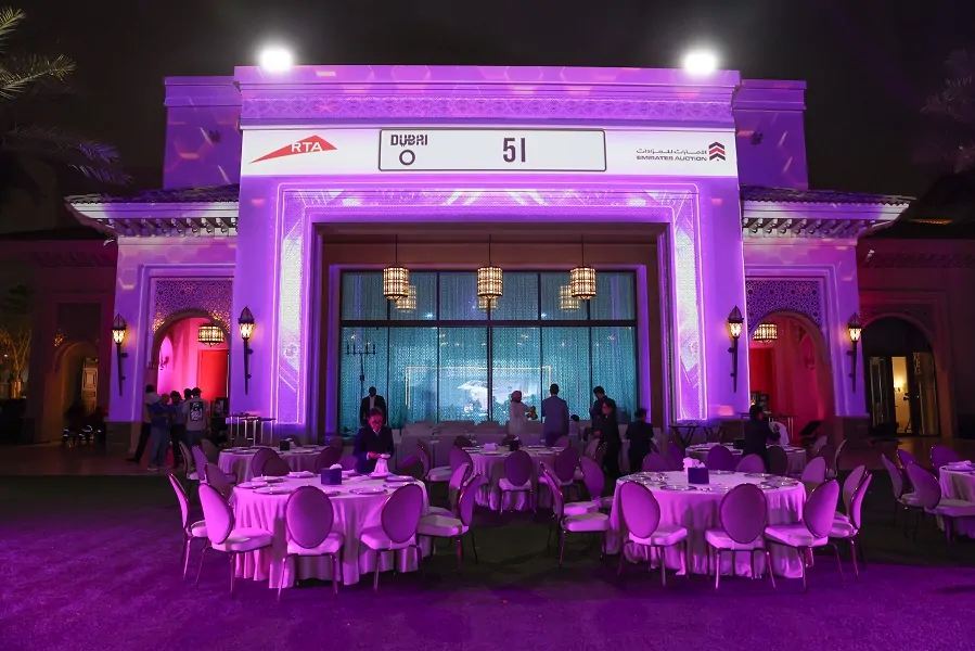 Projection-mapped venue facade showing a featured RTA car plate above dinner tables at the Emirates Auction 2024 by Topaz Events