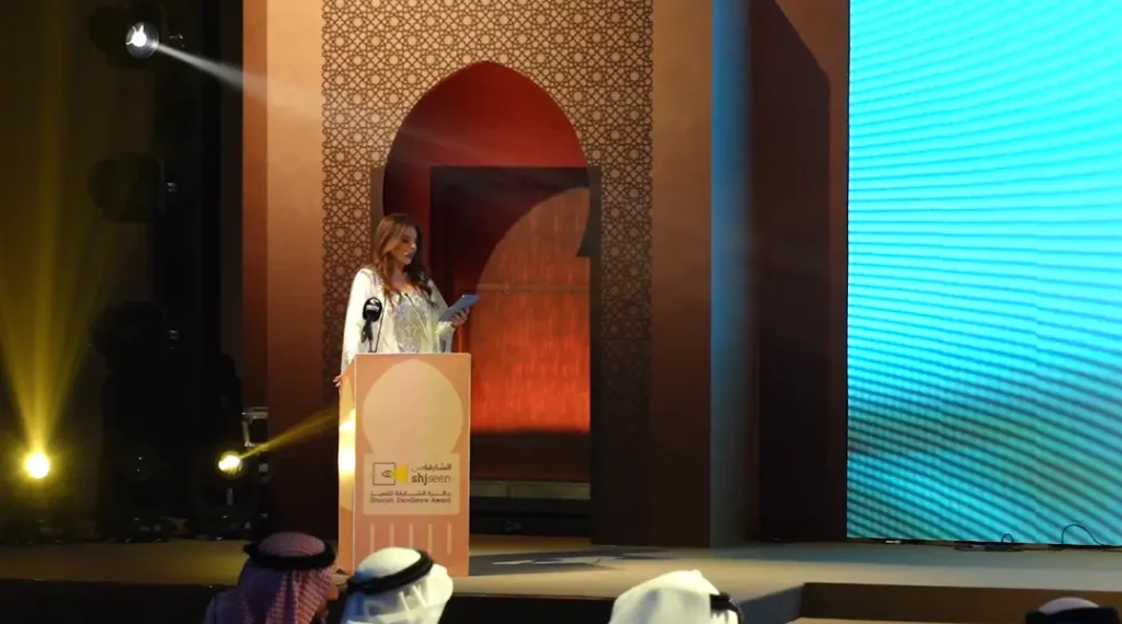 Presenter at the lectern on the arabesque-arch stage at the ShjSeen Sharjah Excellence Award 2023