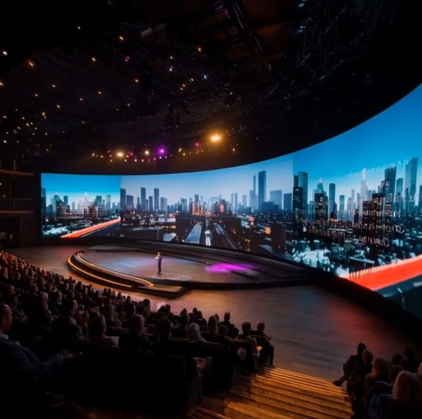 Wide curved LED screen wrapping around a stage with a city skyline, facing a seated audience
