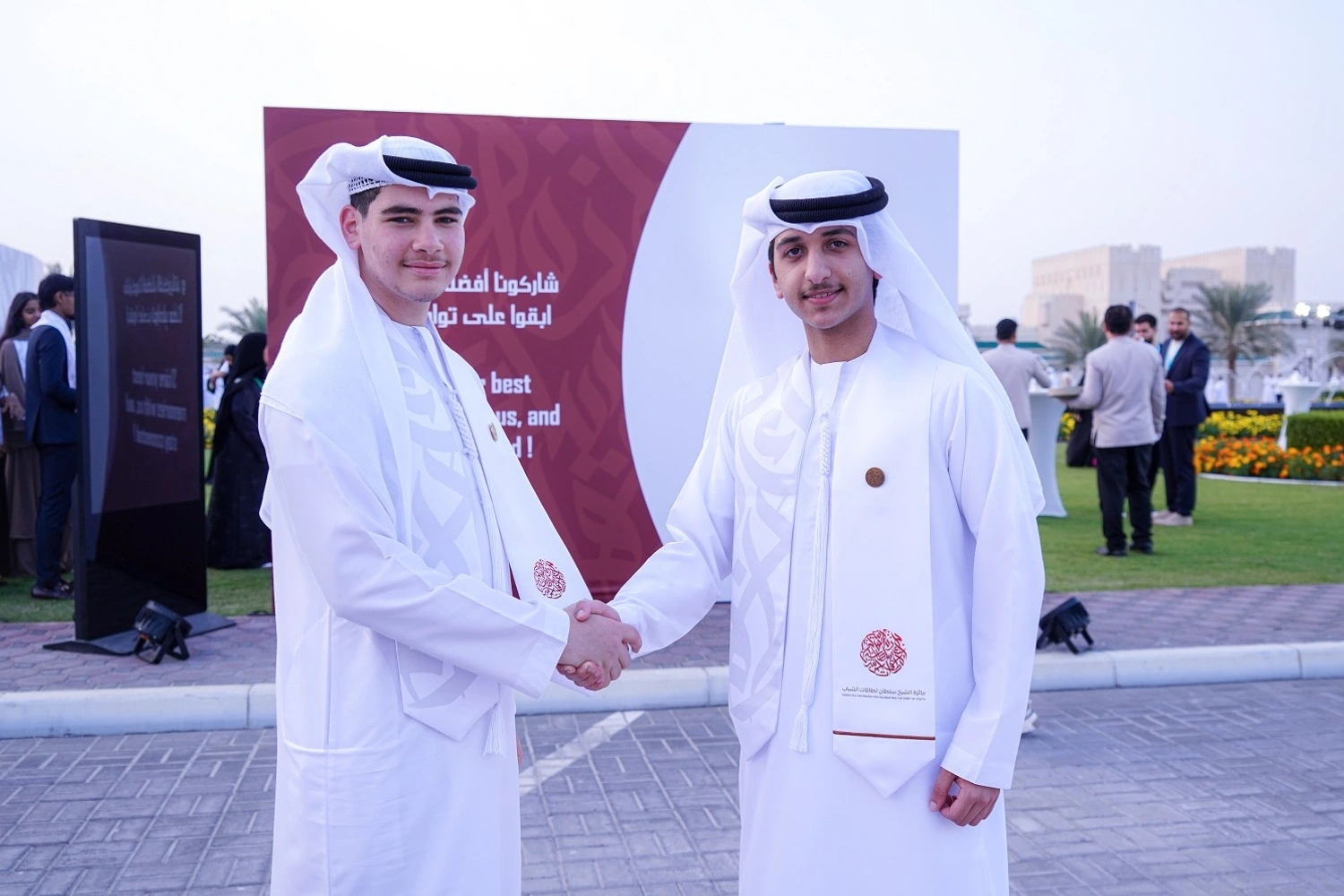 Students gathering to take a picture at the interactive photobooth station, posing in front of the Sheikh Sultan Award branded backdrop.