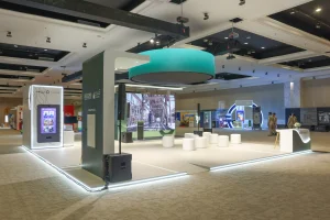 A complete exhibition stand for Sharjah National Oil Corporation featuring a bold curved reception desk, elevated platform flooring, soft-tone architectural finishes, and integrated LED perimeter lighting, designed and delivered by Topaz Events to create a clean, professional, and visually distinctive brand environment at HSE Expo 2026, Al Jawaher, Sharjah.