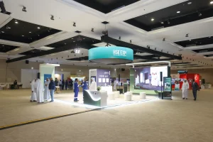 A complete exhibition stand setup for Sharjah National Oil Corporation (SNOC) at the 3rd HSE Expo 2026, Al Jawaher, Sharjah — featuring a curved reception desk, large LED screens, circular overhead branding, and interactive visitor activations, designed and delivered end-to-end by Topaz Events.