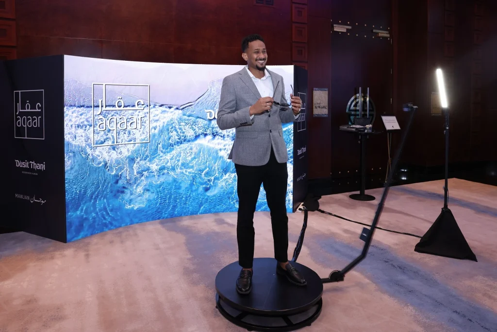 Guest on a 360-degree video booth in front of an Aqaar branded backdrop