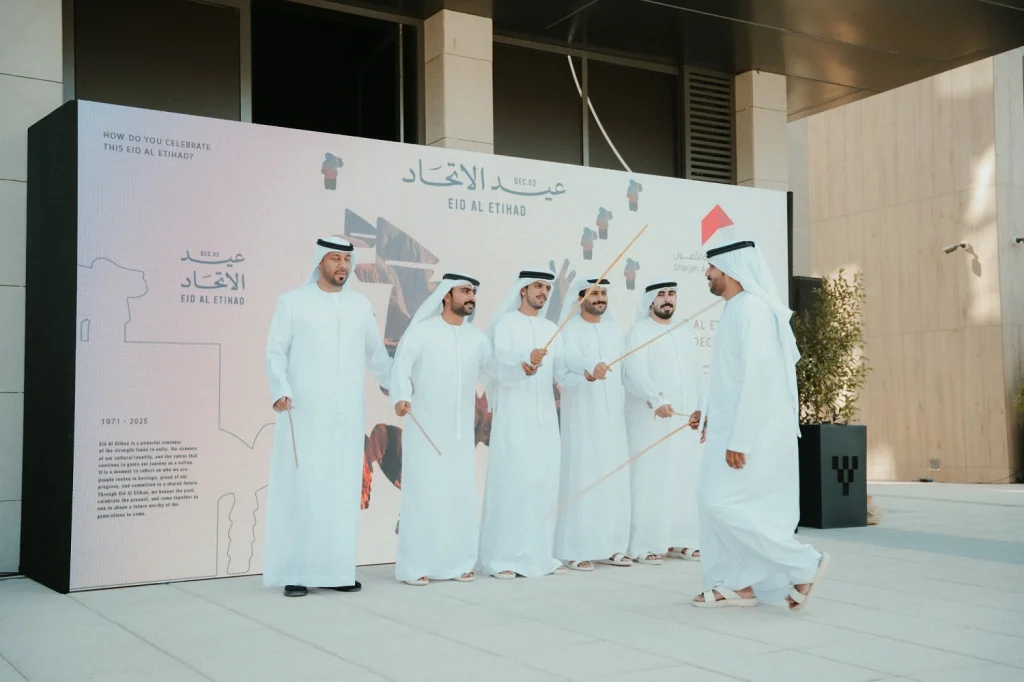 Emirati men performing the traditional Ayala dance in front of a Union-themed backdrop at the 54th UAE National Day event